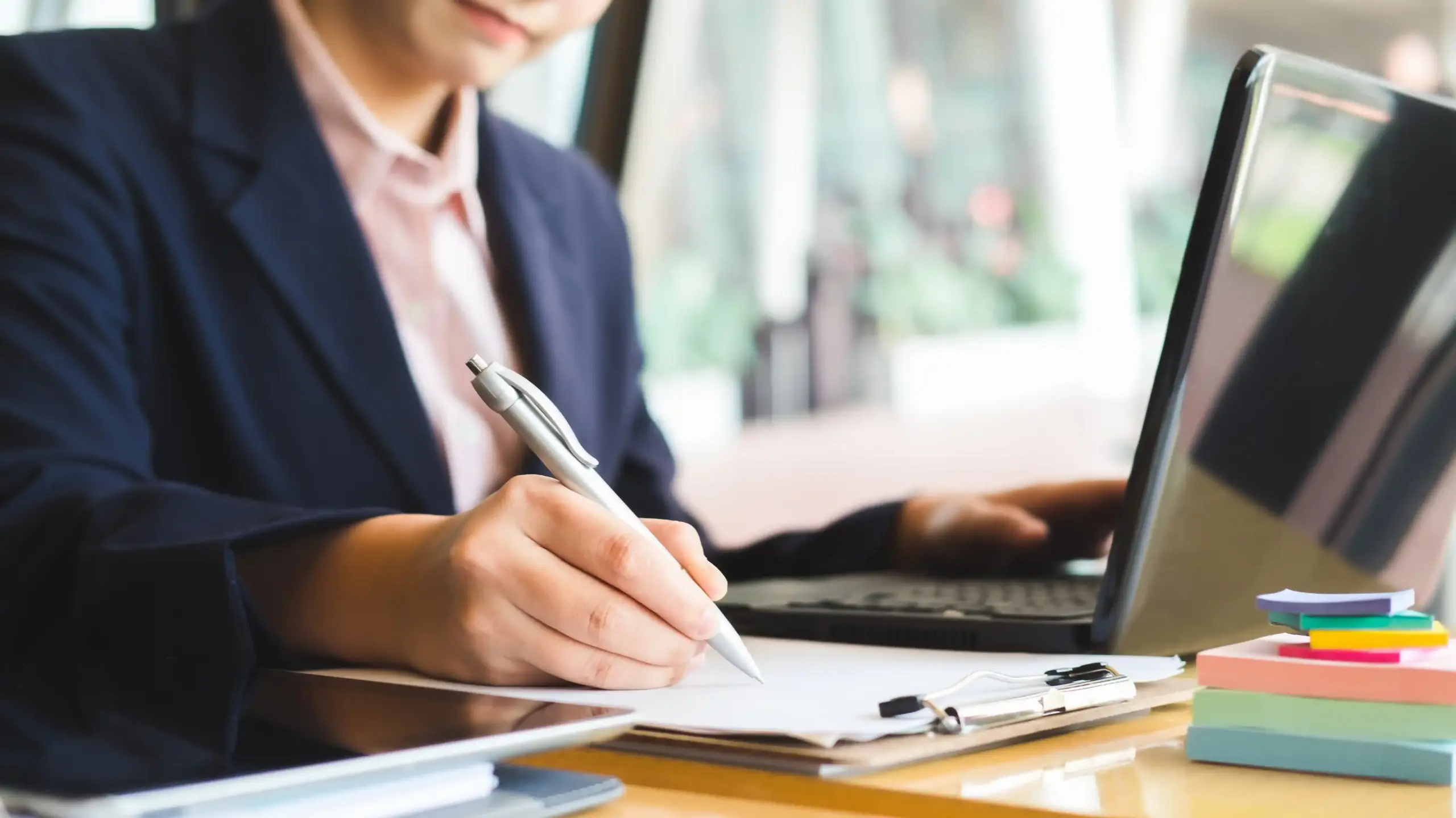 ノートPCを見てメモを取る女性の画像